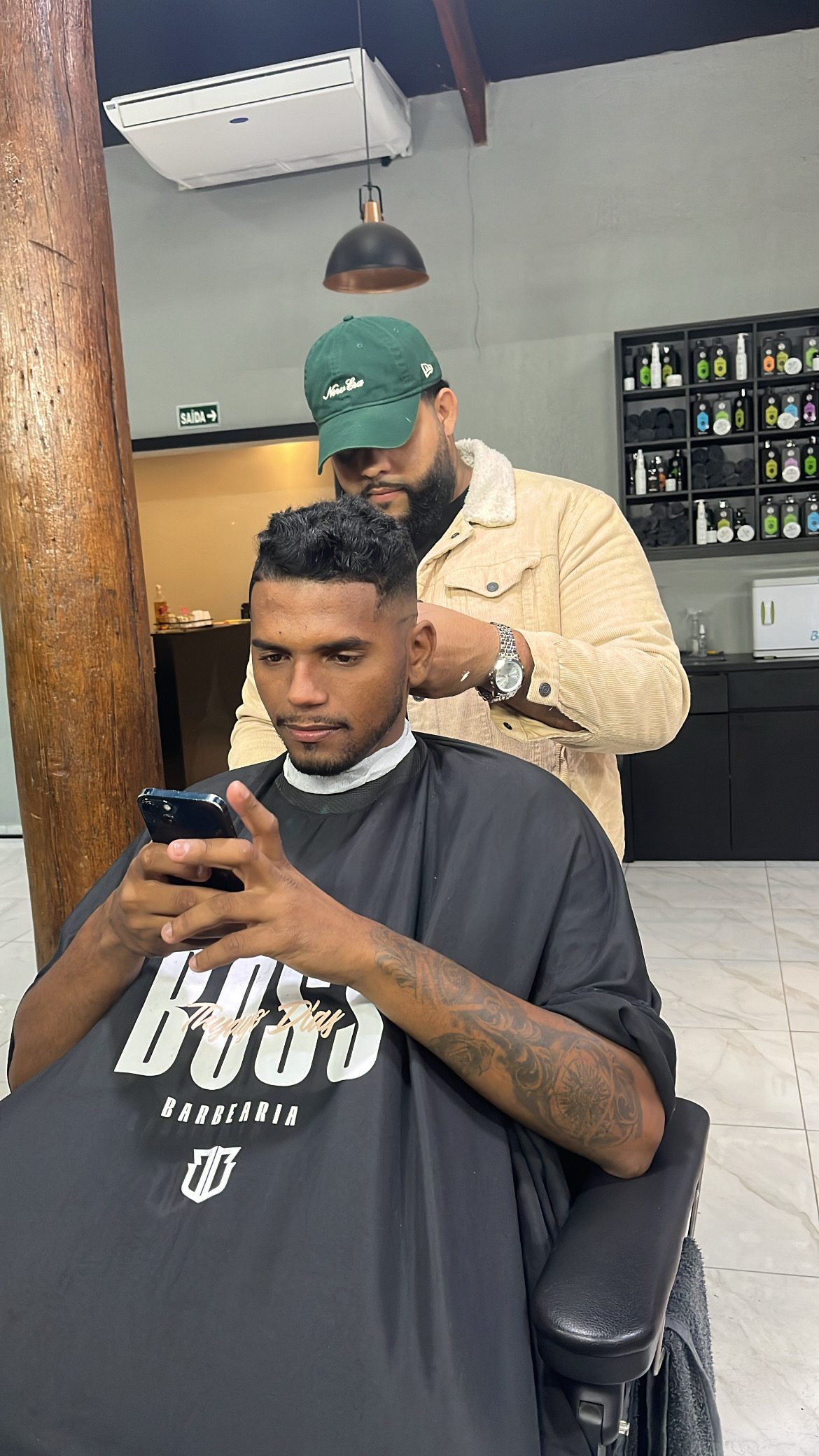 Barbeiro Caíque cortando cabelo com capa The Boss
